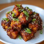 Close-up of crispy, glazed korean braised tofu cubes topped with sesame seeds and sliced green onions.