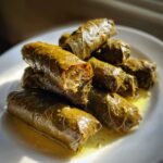 A stack of glistening lemony rice-stuffed grape leaves (dolmades) served in olive oil on a white plate.