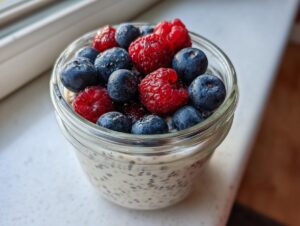 Close-up of a glass jar filled with low calorie chia pudding snack topped generously with fresh blueberries and raspberries.