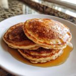 A tempting stack of three golden maple ginger pancakes glistening with syrup on a white plate.