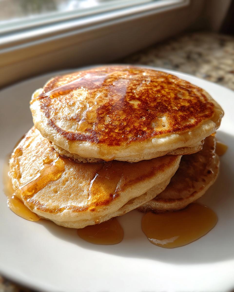 Close-up of a stack of three golden brown maple ginger pancakes generously drizzled with syrup.