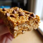 A close-up, macro shot of a chewy oatmeal chocolate chip peanut butter bars held up to the light.