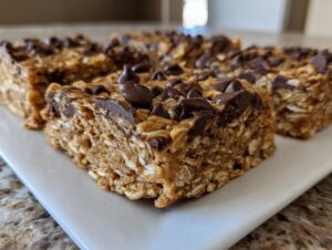 Close-up of thick, chewy oatmeal chocolate chip peanut butter bars topped with melted chocolate chips on a white plate.
