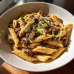 Close-up of a white bowl filled with one-pot creamy beef and garlic butter pasta, topped with parmesan and parsley.