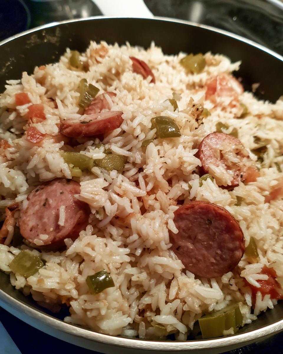 Close-up of one pot sausage and rice mixture with sliced smoked sausage and green peppers in a dark skillet.