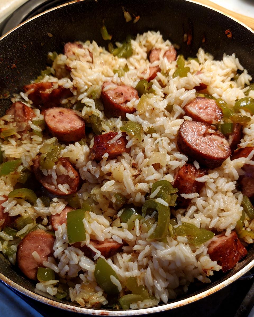 Close-up of one pot sausage and rice mixed with green bell peppers in a dark skillet.