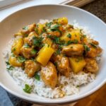 Close-up of a bowl filled with white rice topped with saucy pineapple chicken and garnished with fresh cilantro.