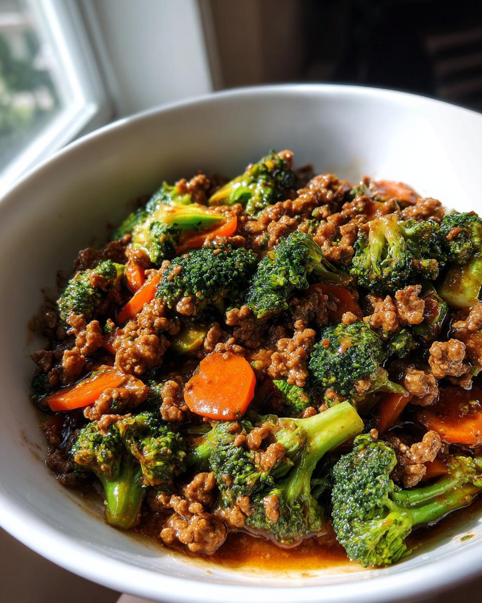 A close-up of a bowl filled with savory ground beef stir fry mixed with bright green broccoli florets and sliced carrots.