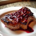 A perfectly seared pork chop topped generously with a thick, glossy raspberry balsamic glazed pork chops sauce.