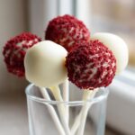 Close-up of red velvet cake pops dipped in white chocolate, some topped with red crumbs.