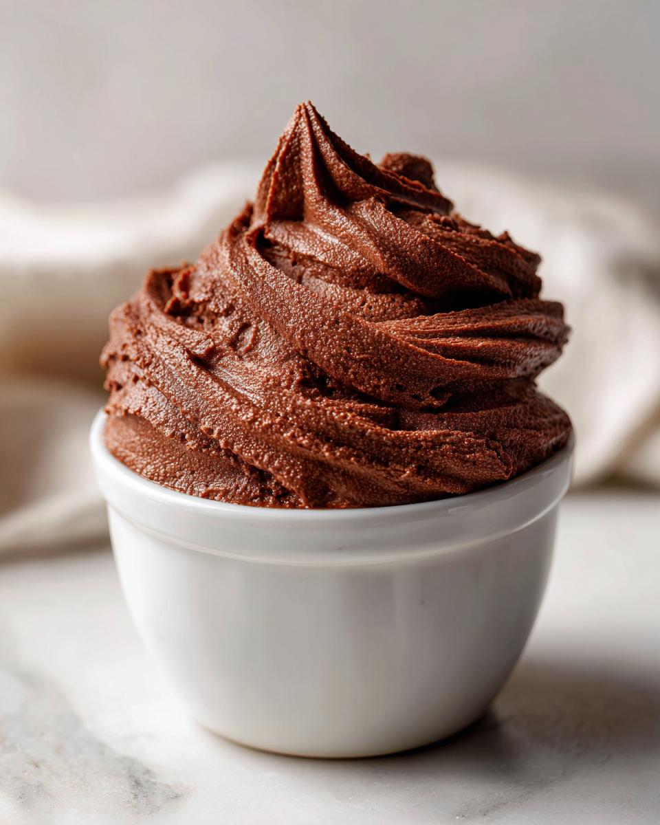 A close-up of rich, dark chocolate mousse piped high into a small white bowl.
