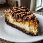 A rich slice of Samoa Cheesecake featuring a dark crust, creamy filling, caramel, chocolate drizzle, and toasted coconut.