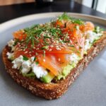 Close-up of a savory protein avocado toast topped with smoked salmon, cottage cheese, and dill.