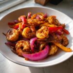 Close-up of seasoned shrimp fajitas mix featuring plump shrimp, bright red and yellow peppers, and vibrant purple onions in a white bowl.