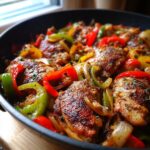 Close-up of perfectly browned chicken scarpariello pieces cooked with vibrant red, green, and yellow bell peppers and onions in a dark skillet.