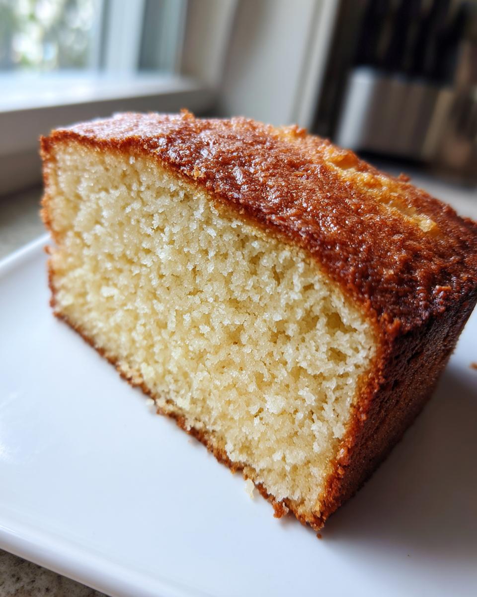 Close-up of a thick slice of moist cream cheese pound cake showing its dense crumb and golden brown, slightly glossy top crust.