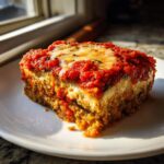 A close-up, sunlit serving of rich eggplant parmesan on a white plate.