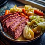 Three thick slices of tender corned beef served alongside boiled cabbage, carrots, and potatoes.