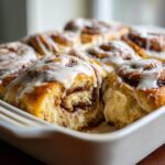 Close-up of gooey sourdough discard cinnamon rolls baked together in a white dish, topped with thick white icing.