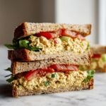 Close-up of a stacked chickpea salad sandwich on whole wheat bread with lettuce and tomato slices.