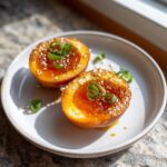 Two halves of a soft-boiled marinated eggs, glistening with sauce and topped with sesame seeds and green onions.