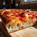 Close-up of a thick slice of Sicilian pizza showing the airy, fluffy interior crust texture.