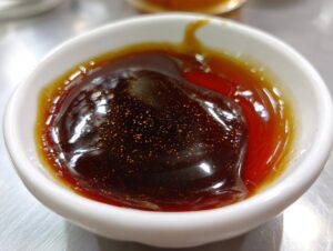 Close-up of thick, glossy japanese teriyaki sauce with visible spices in a small white dipping bowl.