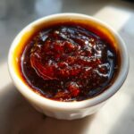 Close-up of thick, dark, glossy homemade japanese teriyaki sauce in a small white dipping bowl.