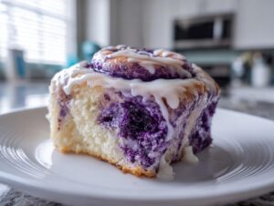 A close-up shot of a single, soft ube cinnamon rolls slice drizzled generously with white vanilla icing.