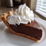 A perfect slice of rich, dark chocolate pie topped with a generous swirl of fresh whipped cream.