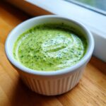 A close-up of vibrant green cilantro lime sauce served in a small white fluted ramekin.