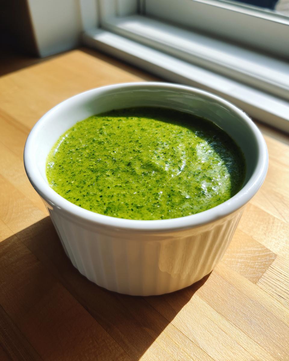 Close-up of bright green cilantro lime sauce served in a small white fluted ramekin on a wooden counter.