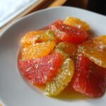 Close-up of a bright citrus salad featuring segments of orange and grapefruit glistening in syrup and sprinkled with zest.