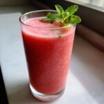 A tall glass filled with a vibrant pink watermelon smoothie, topped with fresh mint leaves.