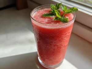 Close-up of a tall glass filled with a vibrant red, icy watermelon smoothie, topped with fresh mint leaves.
