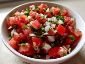 Close-up of a white bowl filled with fresh Authentic pico de gallo, showing diced tomatoes, onions, and cilantro.