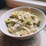 A close-up of creamy Cabbage alfredo mixed with broccoli florets, served in a white bowl and topped with cracked black pepper.