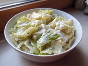 Close-up of a white bowl filled with creamy Cabbage alfredo, featuring wilted cabbage coated in a rich white sauce.