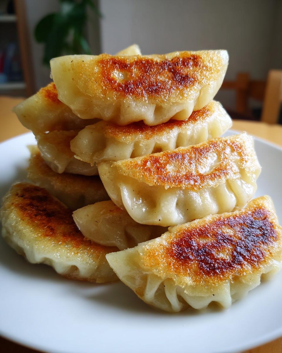 A stack of golden-brown, crispy pan-fried pork cabbage dumplings on a white plate.