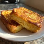 Two thick slices of golden brown, crispy sourdough French toast stacked on a white plate.