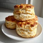 A stack of four golden-brown, tall, and fluffy buttermilk biscuits resting on a white plate.