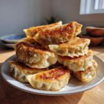 A stack of golden brown, pan-fried Pork Cabbage Dumplings piled high on a white plate, catching bright sunlight.