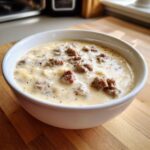 A white bowl filled with creamy Homemade sawmill gravy featuring visible chunks of browned sausage and black pepper.