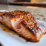 Close-up of a perfectly cooked Honey garlic butter baked salmon fillet with a caramelized, glossy glaze and sesame seeds.