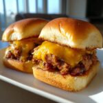 Two delicious leftover meatloaf sliders topped with melted cheddar cheese, served on a white plate.