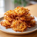 A stack of golden brown, crispy leftover spaghetti fritters piled high on a light-colored plate.