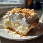 A close-up slice of rich National Coconut Cream Pie topped with whipped cream and toasted coconut flakes.