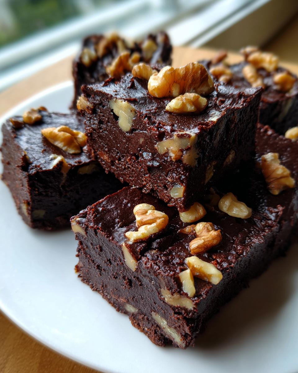 Close-up of rich, dark chocolate Old fashioned nutty fudge squares topped generously with walnut pieces on a white plate.