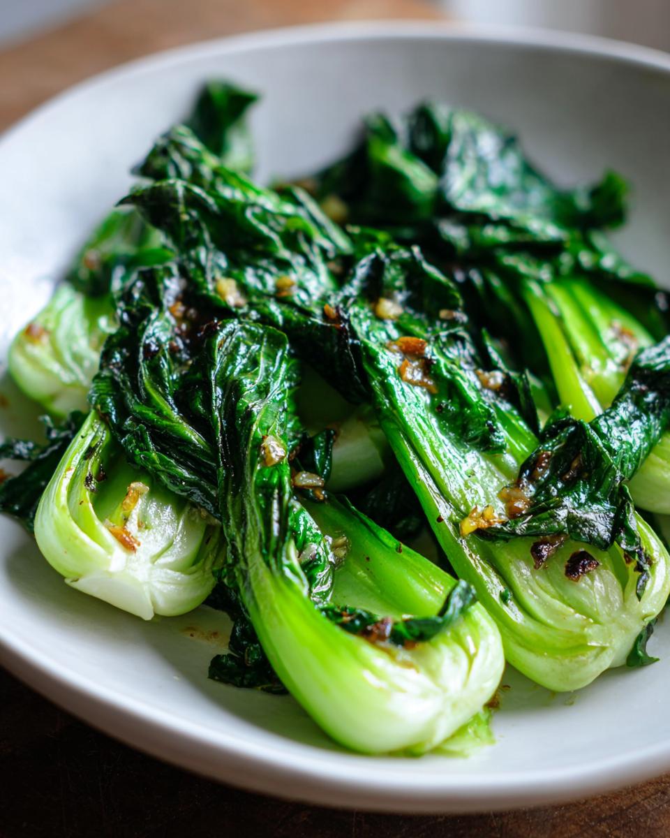 A close-up of vibrant green Sautéed bok choy with garlic served in a white bowl.