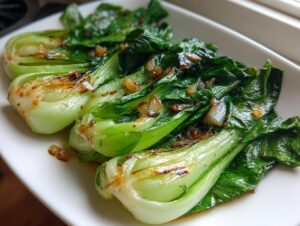 Close-up of perfectly cooked Sautéed bok choy with garlic, glistening with sauce and topped with caramelized onions/garlic bits.